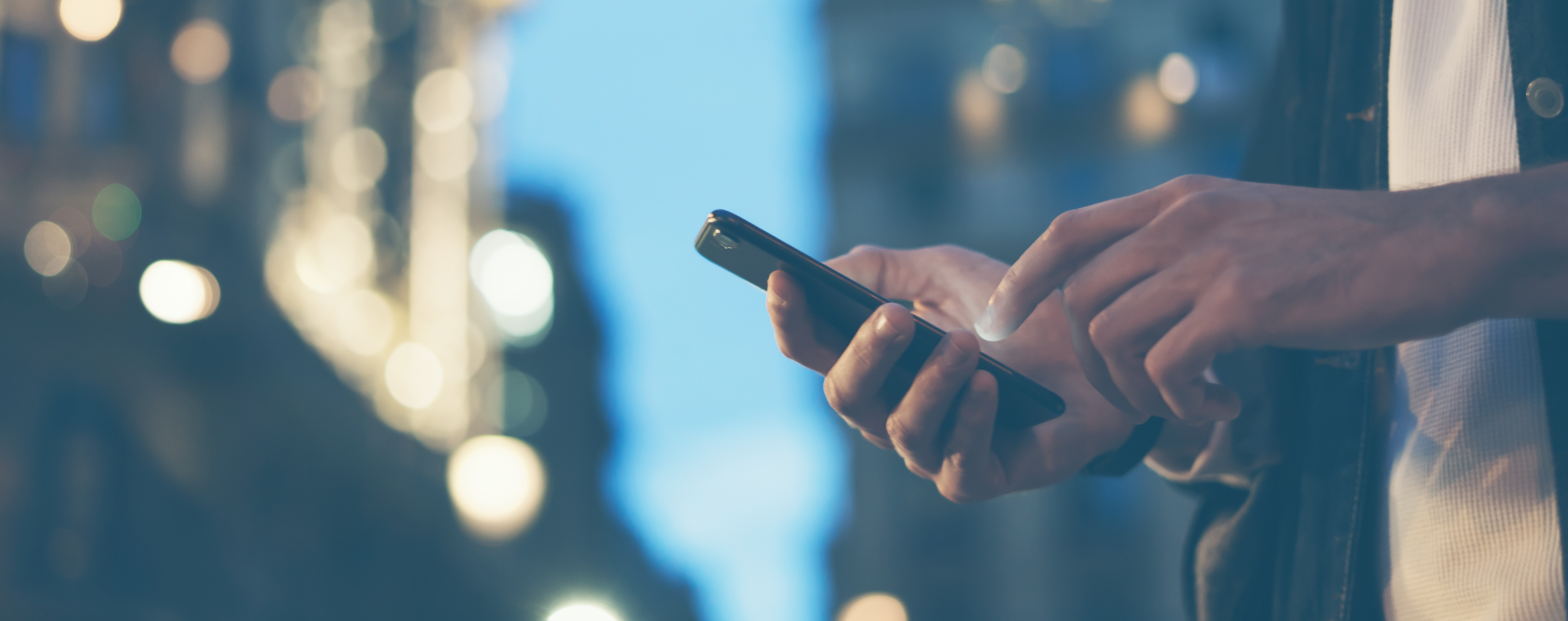 Closeup image of male hands with smartphone at night on city street, searching internet or social networks, hipster man typing an sms message on chat